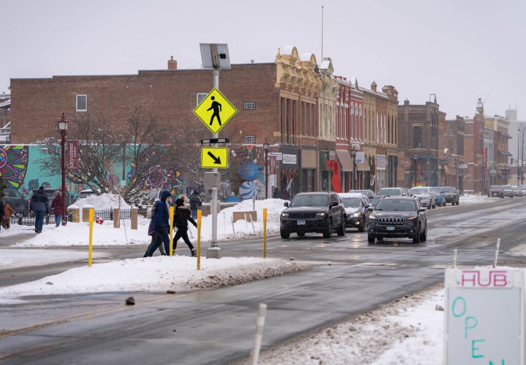 Mankato Riverfront Drive with traffic and people crossing street on a snowy day