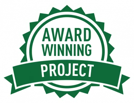 A green badge with white text reading Award Winning Project. The design features a circular shape with jagged edges and a banner across the center.