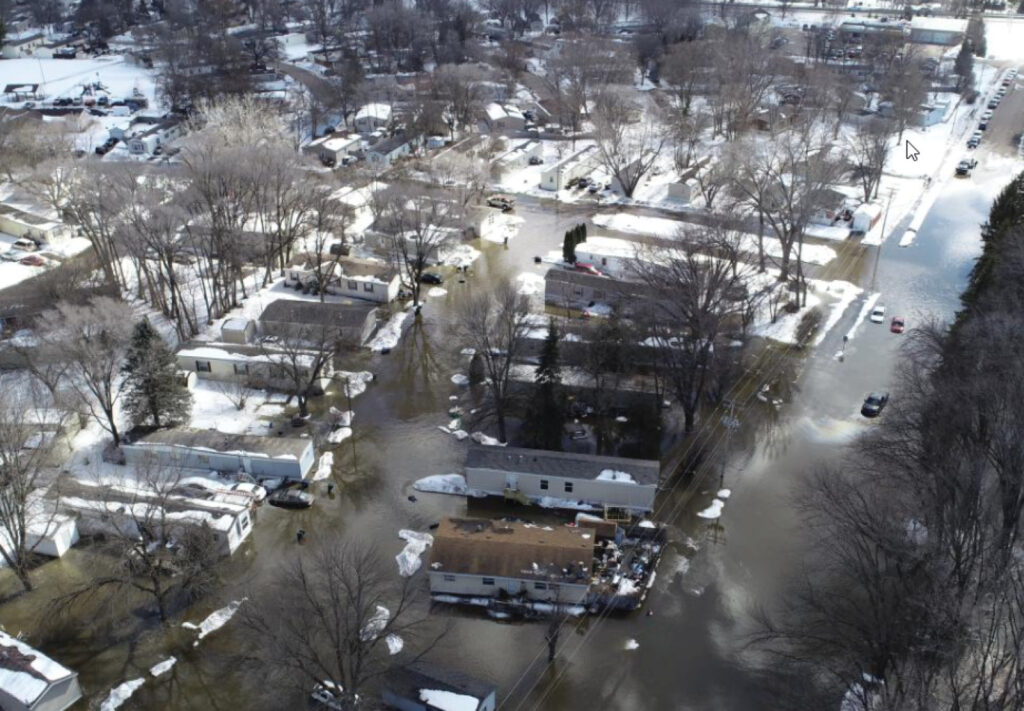 Aerial view of a residential neighborhood with flooded streets and yards. Snow covers the ground and rooftops, while water surrounds homes and vehicles—captured by NexTech: Using UAVs for Flood Analysis in a severe winter flood setting.