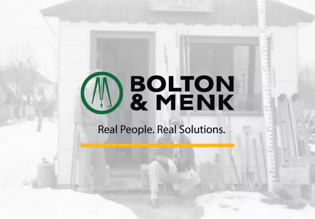 Two men in front of a Garage with the Bolton & Menk logo in front
