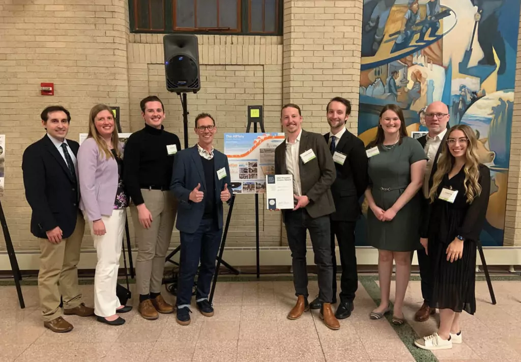 Group of people standing by project panel holding a certificate