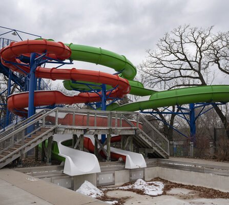 Two colorful waterslides, one orange and one green, stand tall amidst a snowy pool during winter.
