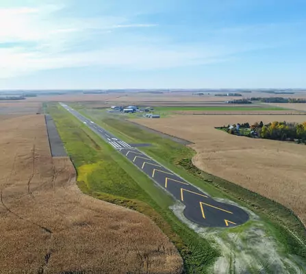 Aerial view of a rural runway with yellow lines, surrounded by fields.