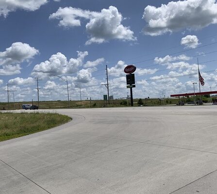 Road in front of gas station with power lines, under a blue sky with clouds