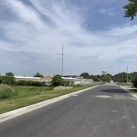 Freshly paved road with buildings and greenery, water tower in the background