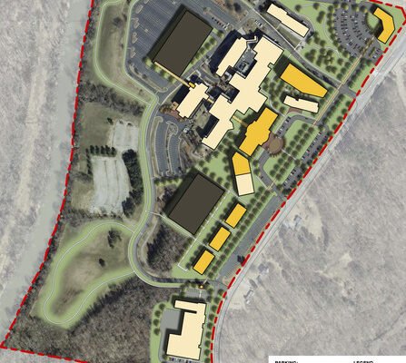 Aerial view of a large campus plan surrounded by trees, with multiple buildings in various colors. Roads and parking lots are visible, and paths connect the structures. A red dashed line marks the boundary. A legend explains the color coding.