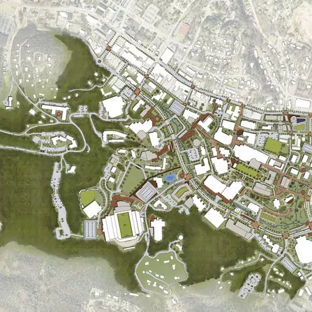 Aerial view of a detailed urban landscape map, featuring various buildings, sports fields, parking lots, and roads. Green areas surround a complex network of streets and structures, indicating a mix of urban and natural spaces.