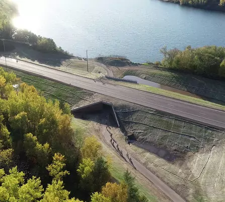 Arial view of bikers on a trail, passing through a tunnel beneath a highway.