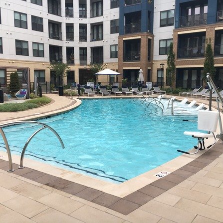 Outdoor pool with lounge chairs, umbrellas, and a modern apartment complex in the background.