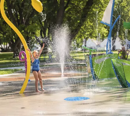 Children playing in a colorful community splash pad with various water features