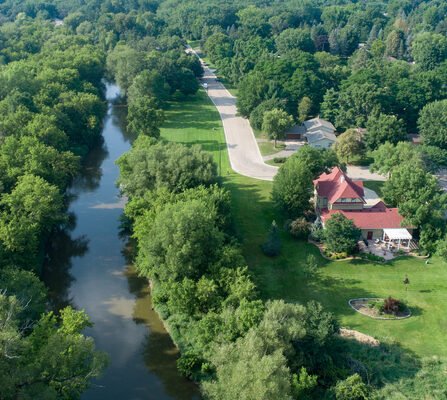 Arial view of river, road, forest, and houses. A red-roofed house stands out among the others