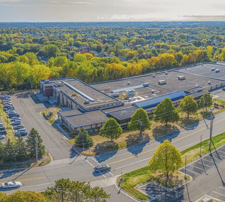 Aerial view of a spacious building and car-filled parking lot, surrounded by an abundance of trees