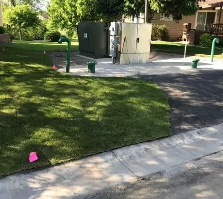 A water lift station with green pipes protruding from the ground and a silver control box, situated amidst residential houses