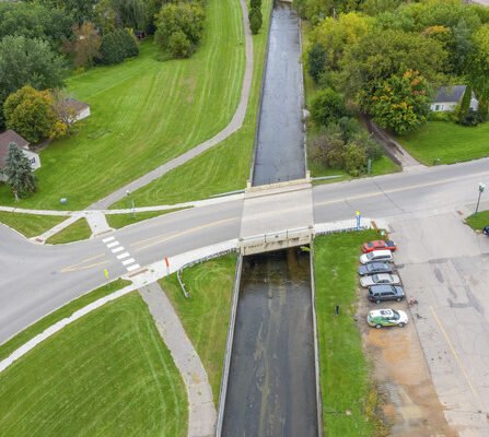 A bird's-eye view of a road intersection, featuring a bridge over a river, with roads and sidewalks