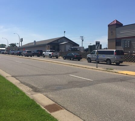 Cars lined up on a road with buildings in the background