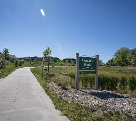 Sidewalk with bench and park sign in a residential area surrounded by native grass and trees