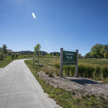 Sidewalk with bench and park sign in a residential area surrounded by native grass and trees