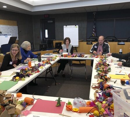 A group of individuals sitting around a table, working together and using craft materials to create visual aids