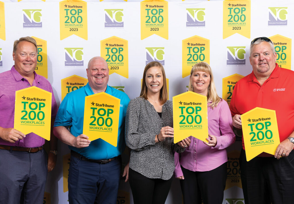 Five people smile and hold yellow flags boasting the Star Tribune Top 200 Workplaces 2023 accolade. Against a backdrop of repeating logos, three men wear red, blue, and striped shirts while two women sport black and purple tops, celebrating their 2023 Top 200 Workplace honor.