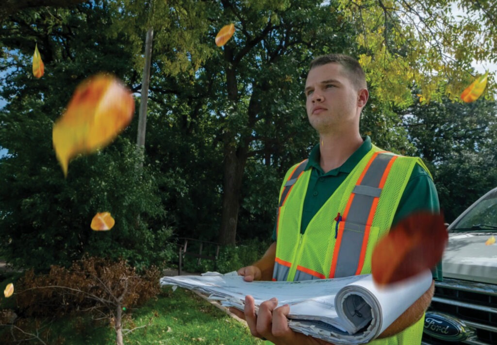 Man outside in safety vest holding a set of papers.