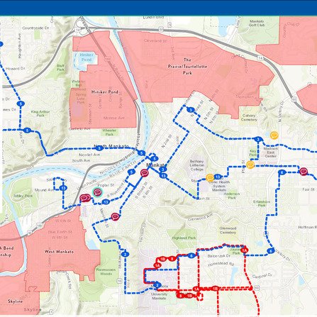 A detailed map showing a city layout with blue, red, and green dotted paths overlaying streets and neighborhoods. Pink shaded areas indicate different zones. Major landmarks and parks are labeled, with a river running through the city.