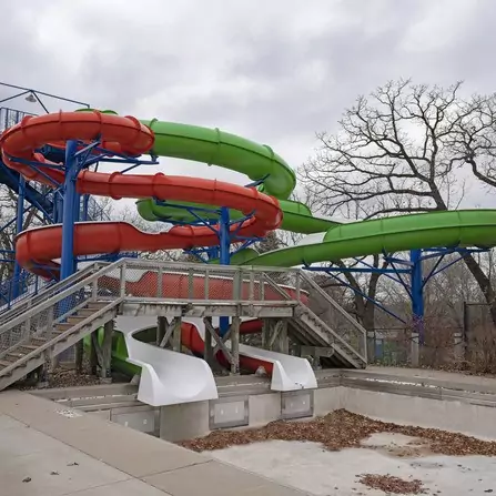 Two colorful waterslides, one orange and one green, stand tall amidst a snowy pool during winter.