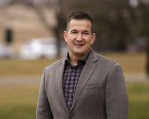 Man in brown suit jacket smiling at camera