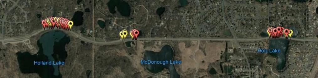 A satellite map displays three lakes—Holland, McDonough, and Holz—linked by a road dotted with various colored pins, marking points of interest. Intriguingly, wildlife crossings are strategically placed along this route to facilitate safe animal movement.