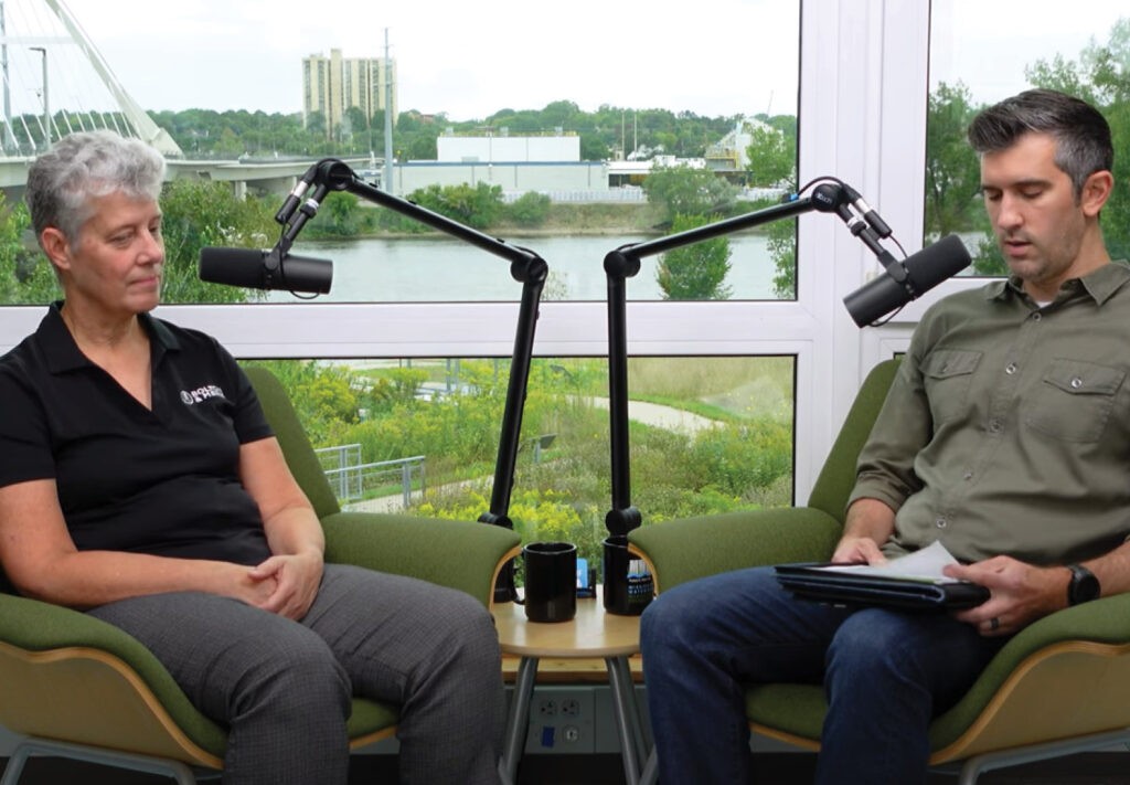 Two people sitting with microphones for a podcast