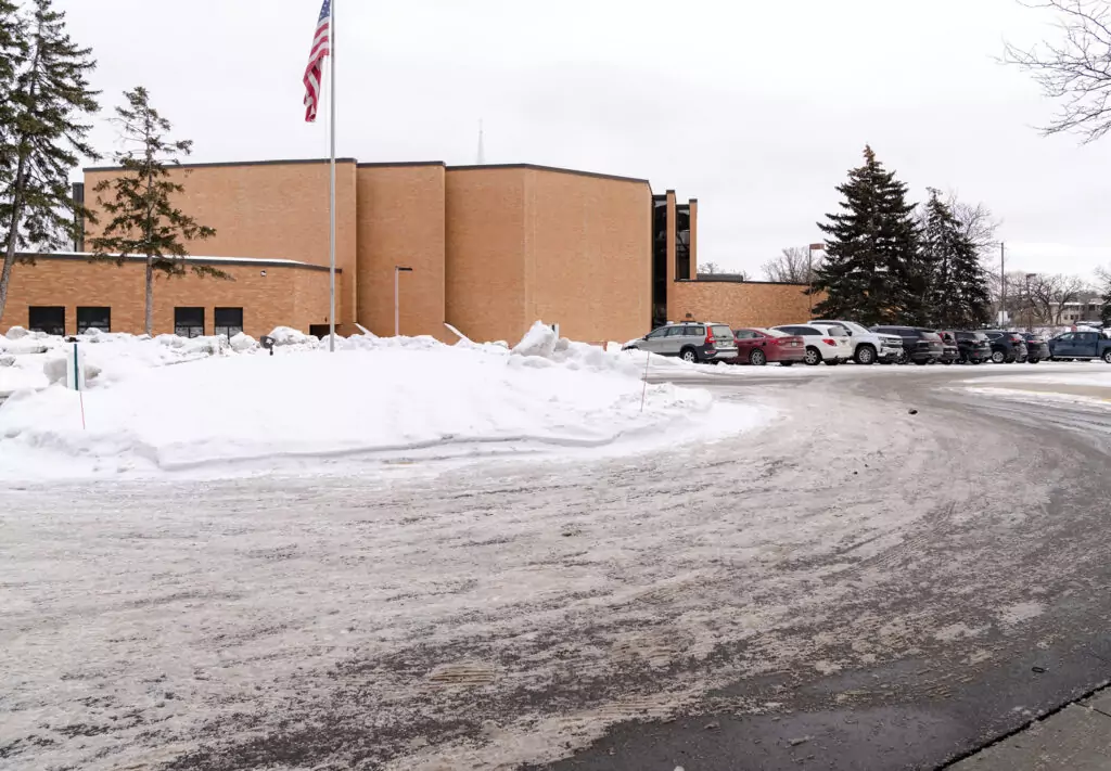 A road with slushy snow on it and building with cars parked in front of it in the background