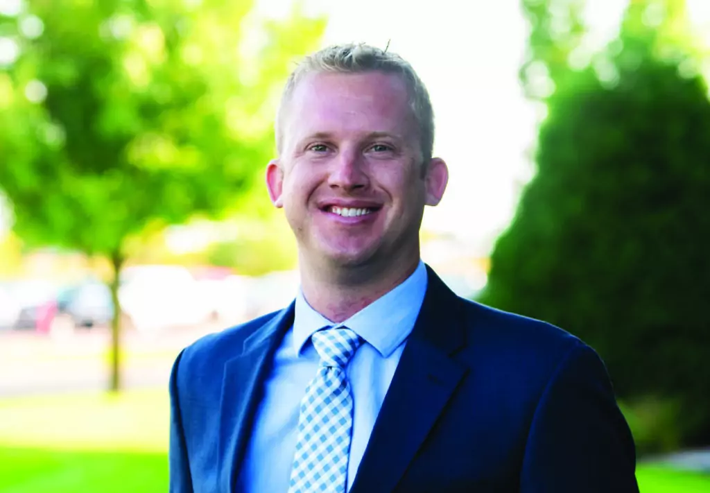 Professional headshot of a man in a dark blue jacket and light blue button up shirt