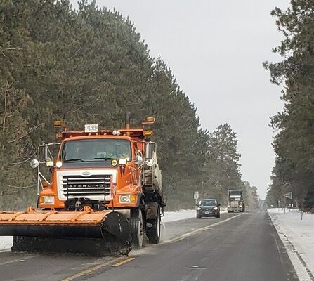 A snow plow on the road with conifers