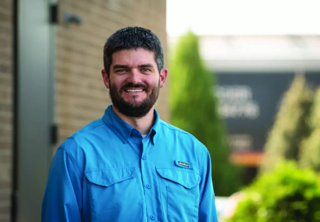 Outdoor headshot of a man with a teal collared shirt