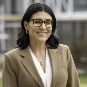 Headshot of a brunette woman wearing glasses, a tan cardigan, and white blouse