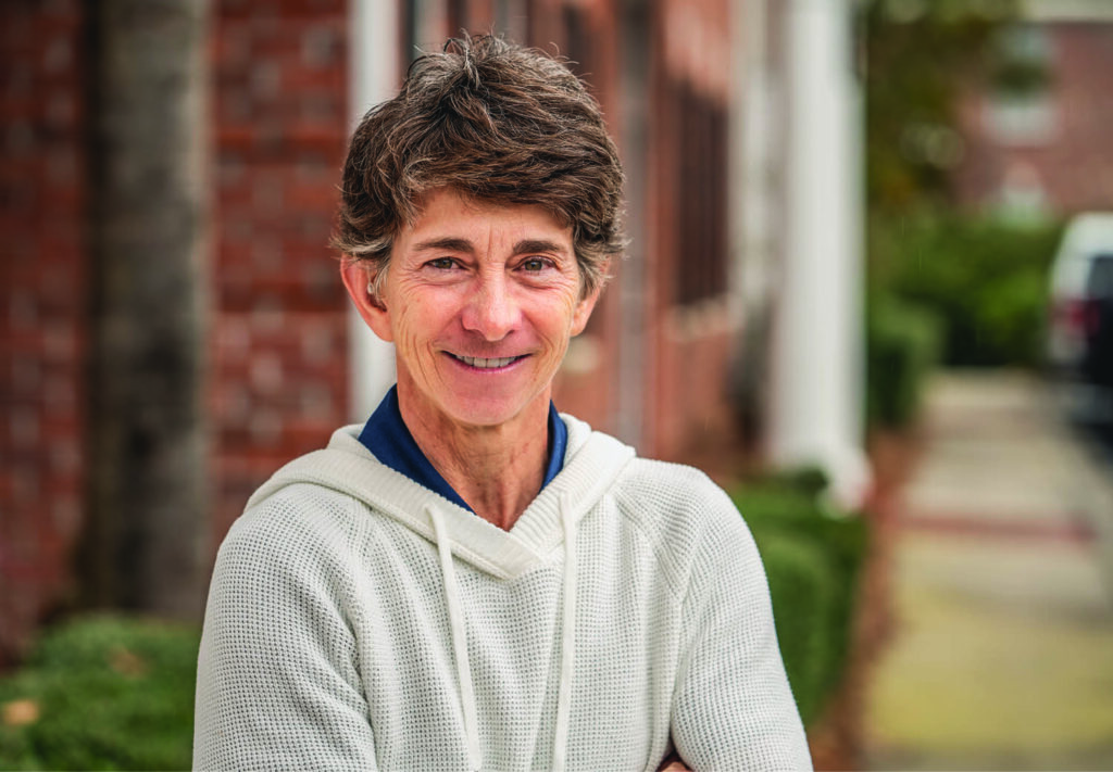 • Headshot photo of a woman with salt and pepper hair wearing a beige pullover sweater