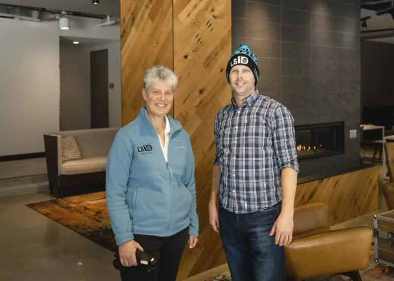 A person in a blue zip-up and a person in a flannel shirt with beanie hat looking at camera and smiling