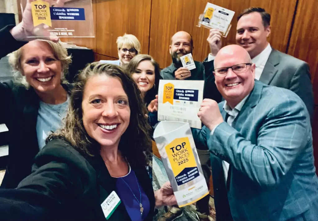 A group of smiling people in business attire celebrate together, holding plaques and signs that read Top Workplaces 2023.