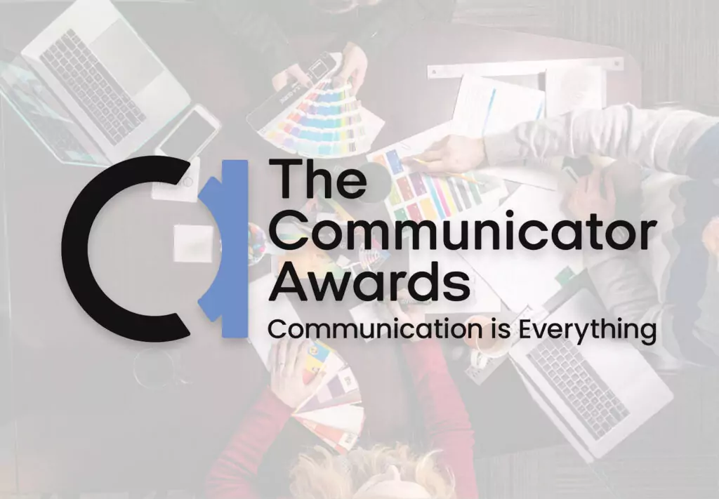 Overhead view of people working with laptops, papers, and color swatches at a table. Overlaid text reads: The Communicator Awards. Communication is Everything with a logo on the left.