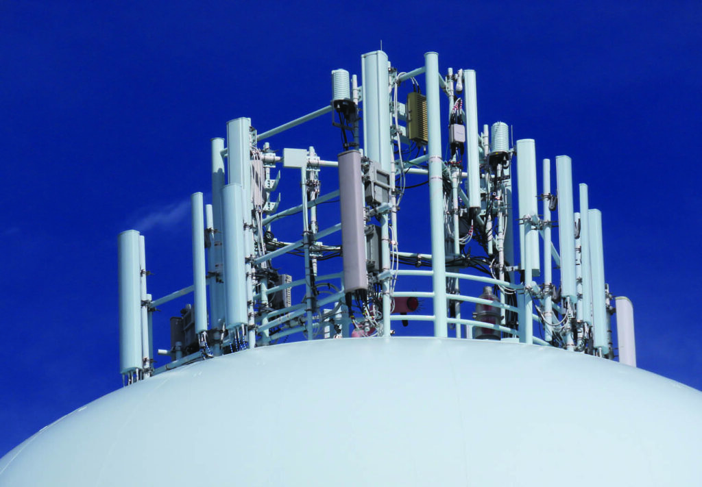 Close-up of a white dome structure topped with numerous antennas and communication equipment, highlighting its role in telecommunication services against a clear blue sky.