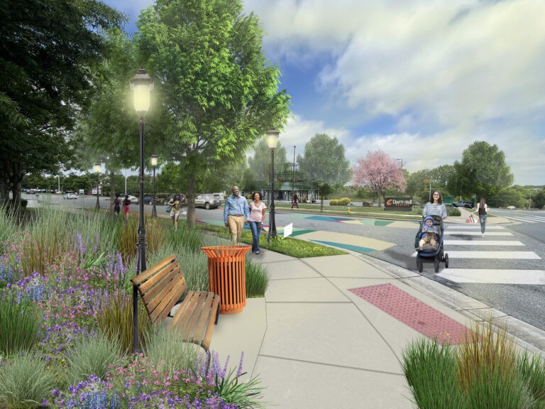 A landscaped urban sidewalk with benches, flowers, and trees. Several people walk, including a woman pushing a stroller and a couple talking. A crosswalk and cars are visible in the background under a partly cloudy sky.