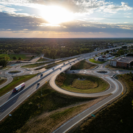 Aerial view of a highway interchange at sunset, with cars and a truck navigating roundabouts and overpasses