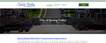 Screenshot of the City of Spring Valley, Minnesota website homepage, featuring a street view and navigation bar with links for documents, departments, and contacts. The main headline reads City of Spring Valley.