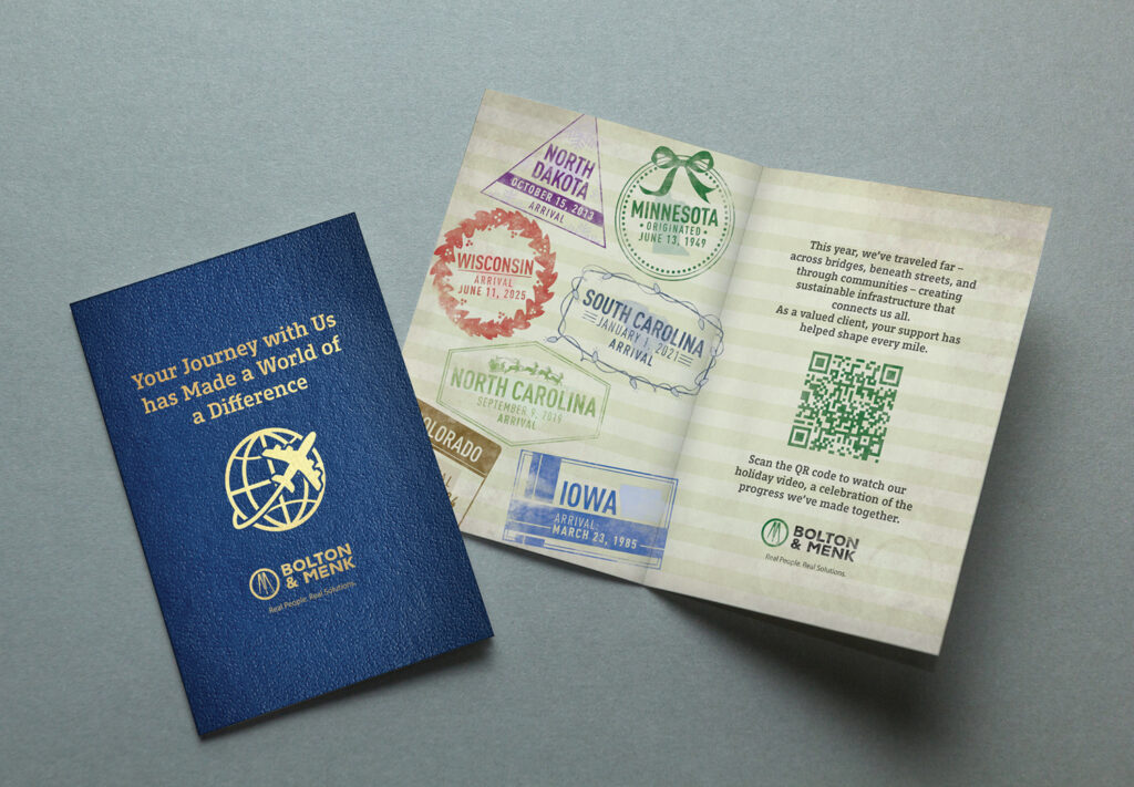 A blue booklet with gold text and a globe icon sits next to an open card displaying colorful state stamps, a QR code, and travel-themed text. Both items are on a gray surface.