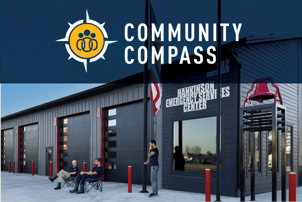 Three people sit and talk outside a modern emergency services center with red garage doors and American flags. Text highlight reads, Community Compass.