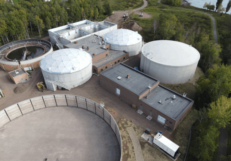 Large white tanks at a wastewater treatment facility along the water.