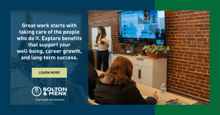 A woman gives a presentation to a small group in a modern conference room. A large sign reads, “Great work starts with taking care of the people who do it…” featuring the Bolton & Menk logo and highlighting the Wahlbrink Grassroots Leadership Award.