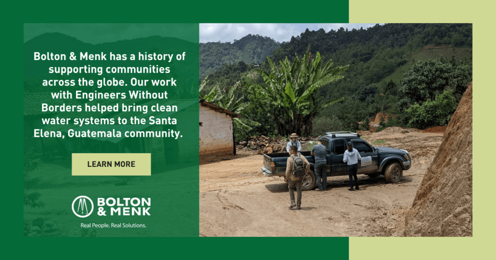 Three people stand near a pickup truck in a rural, mountainous area with lush greenery and simple buildings. A text overlay highlights Bolton & Menk’s clean water project and engineering mentorship in Santa Elena, Guatemala.