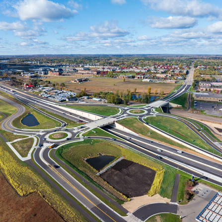 Aerial view of a completed roadway interchange featuring roundabouts, bridge crossings, and improved highway connections near commercial development