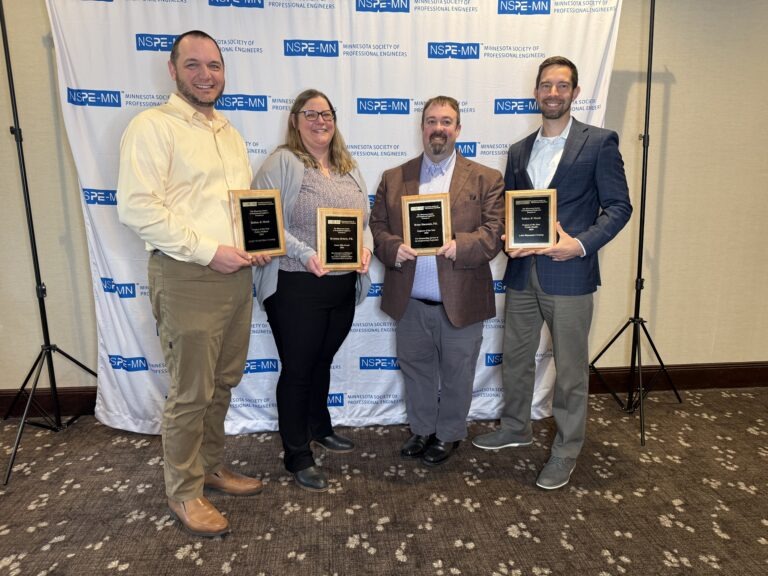 Four people stand side by side, smiling and holding MnSPE Project Awards plaques in front of a backdrop with the NSPE-MN logo at a professional event.
