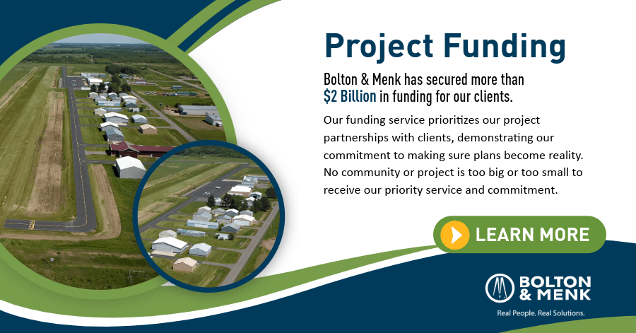 Aerial view of a rural area with buildings and roads on the left, overlaid with text about Bolton & Menk securing over $2 billion in project funding, and a green Learn More button on the right.